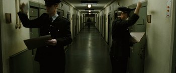 Movie still from “Hunger” (2008), directed by Steve McQueen – Two men in black suits are standing in a long hallway; Wide shot, Low angle