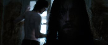 Movie still from “Hunger” (2008), directed by Steve McQueen – A man with long black hair is in a dark room; Close Up shot, Over the shoulder angle