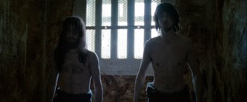 Movie still from “Hunger” (2008), directed by Steve McQueen – Two shirtless men standing next to each other in front of a window; Medium shot, Low angle