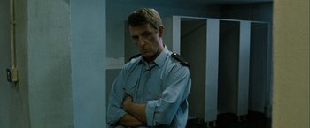 Movie still from “Hunger” (2008), directed by Steve McQueen – A man in a uniform standing with his arms crossed; Medium shot, Low angle