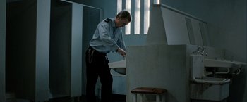 Movie still from “Hunger” (2008), directed by Steve McQueen – A man in a prison uniform standing next to a sink in a room; Medium shot, Low angle