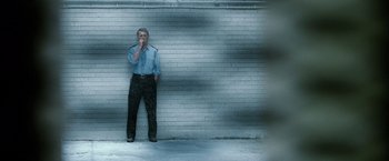 Movie still from “Hunger” (2008), directed by Steve McQueen – A man standing in front of a brick wall with his hand to his mouth; Wide shot, Low angle