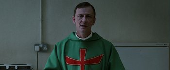 Movie still from “Hunger” (2008), directed by Steve McQueen – A man in a green and red robe with a cross on it; Close Up shot, Low angle