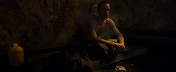 Movie still from “Hunger” (2008), directed by Steve McQueen – A shirtless man sitting on a bed in a dark room; Medium shot, High angle