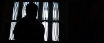 Movie still from “Hunger” (2008), directed by Steve McQueen – A person standing next to a window in the dark; Close Up shot, Low angle