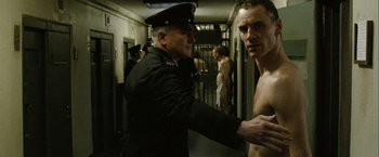 Movie still from “Hunger” (2008), directed by Steve McQueen – A man in a military uniform standing next to another man in a jail cell; Medium shot, Over the shoulder angle