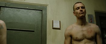 Movie still from “Hunger” (2008), directed by Steve McQueen – A man standing in front of a door in a room; Close Up shot, Low angle