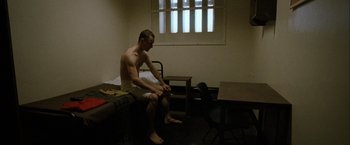 Movie still from “Hunger” (2008), directed by Steve McQueen – A man sitting on top of a bed in a room; Wide shot, High angle