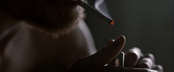 Movie still from “Hunger” (2008), directed by Steve McQueen – A person is smoking a cigarette in a dark room; Extreme Close Up shot, Overhead angle