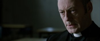 Movie still from “Hunger” (2008), directed by Steve McQueen – An older man in a black shirt is looking at the camera; Close Up shot, Over the shoulder angle