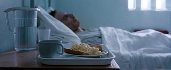 Movie still from “Hunger” (2008), directed by Steve McQueen – A man in bed with a plate of food on a tray; Medium shot, High angle