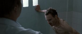 Movie still from “Hunger” (2008), directed by Steve McQueen – A man leaning up against a wall in a bathroom; Medium shot, Over the shoulder angle
