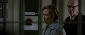 Movie still from “Hunger” (2008), directed by Steve McQueen – A woman in a gray coat is sitting in a room; Close Up shot, Over the shoulder angle