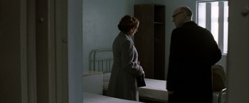Movie still from “Hunger” (2008), directed by Steve McQueen – A woman standing in a room next to a bed; Medium shot, Over the shoulder angle