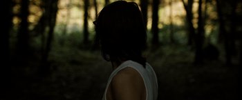 Movie still from “Hunger” (2008), directed by Steve McQueen – A woman in a white tank top in the woods; Close Up shot, Over the shoulder angle