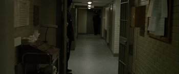 Movie still from “Hunger” (2008), directed by Steve McQueen – A person standing in a dark hallway next to a jail cell; Wide shot, High angle