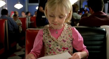 Movie still from “I Am Sam” (2001), directed by Jessie Nelson – A little girl sitting in a chair reading a book; Close Up shot, Over the shoulder angle
