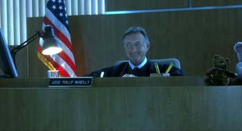 Movie still from “I Am Sam” (2001), directed by Jessie Nelson – A man sitting in a judge's chair in front of the american flag; Medium shot, Low angle