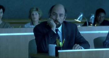 Movie still from “I Am Sam” (2001), directed by Jessie Nelson – A man sitting at a table with a pen in his mouth; Medium shot, Over the shoulder angle