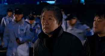 Movie still from “I Saw the Devil” (2010), directed by Jee-woon Kim – An older man in a black jacket is in front of a group of police officers; Close Up shot, Over the shoulder angle