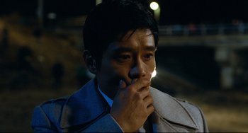 Movie still from “I Saw the Devil” (2010), directed by Jee-woon Kim – A man in a suit is holding his hand to his face; Close Up shot, Over the shoulder angle