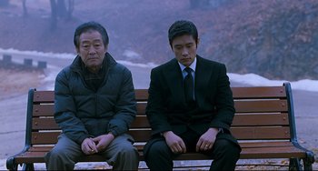 Movie still from “I Saw the Devil” (2010), directed by Jee-woon Kim – Two men sitting on a wooden park bench; Medium shot, Over the shoulder angle