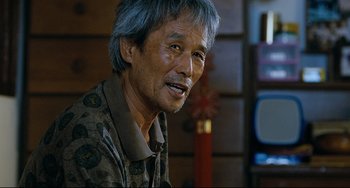 Movie still from “I Saw the Devil” (2010), directed by Jee-woon Kim – An older man with gray hair is sitting in front of a television; Close Up shot, Over the shoulder angle