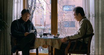 Movie still from “I Saw the Devil” (2010), directed by Jee-woon Kim – Two men are sitting at a table in front of a window; Medium shot, High angle