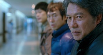 Movie still from “I Saw the Devil” (2010), directed by Jee-woon Kim – A group of men standing next to each other in a hallway; Close Up shot, Over the shoulder angle
