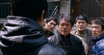 Movie still from “I Saw the Devil” (2010), directed by Jee-woon Kim – A group of men standing next to each other on the street; Medium shot, Over the shoulder angle