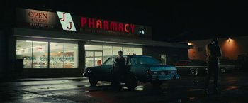 Movie still from “I'm Your Woman” (2020), directed by Julia Hart – A woman standing in front of a car in front of a pharmacy; Extreme Wide shot, Low angle