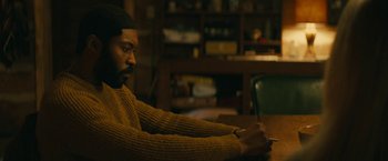 Movie still from “I'm Your Woman” (2020), directed by Julia Hart – A man sitting at a wooden table in front of a book case; Medium shot, Over the shoulder angle