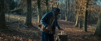 Movie still from “I'm Your Woman” (2020), directed by Julia Hart – An old man in a hat and jacket is lighting a candle on a tree stump; Medium shot, Low angle