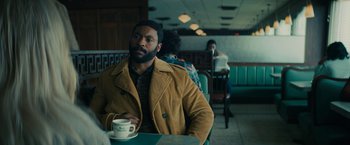 Movie still from “I'm Your Woman” (2020), directed by Julia Hart – A man sitting at a table with a cup of coffee; Medium shot, Over the shoulder angle