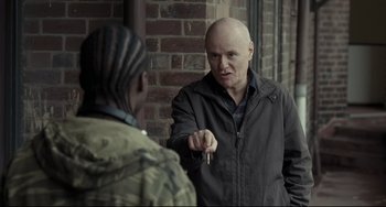 Movie still from “I, Daniel Blake” (2016), directed by Ken Loach – A bald man holding a key in front of another bald man; Medium shot, Over the shoulder angle