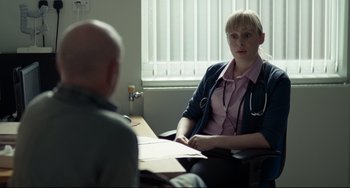 Movie still from “I, Daniel Blake” (2016), directed by Ken Loach – A woman sitting in front of a man in front of a table; Medium shot, Over the shoulder angle