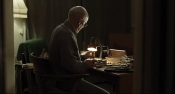 Movie still from “I, Daniel Blake” (2016), directed by Ken Loach – An older man sitting at a desk looking at a book; Medium shot, Low angle