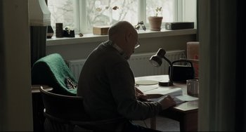 Movie still from “I, Daniel Blake” (2016), directed by Ken Loach – An older man sitting at a table reading a book; Medium shot, Over the shoulder angle