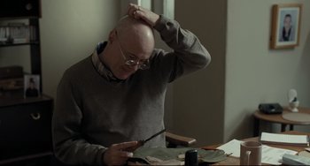 Movie still from “I, Daniel Blake” (2016), directed by Ken Loach – An older bald man sitting at a table looking at a piece of paper; Medium shot, Over the shoulder angle