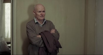 Movie still from “I, Daniel Blake” (2016), directed by Ken Loach – An older man holding his arms crossed while wearing a sweater; Medium shot, Over the shoulder angle