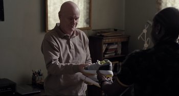 Movie still from “I, Daniel Blake” (2016), directed by Ken Loach – An older bald man holding a pair of shoes; Medium shot, Over the shoulder angle