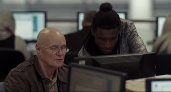 Movie still from “I, Daniel Blake” (2016), directed by Ken Loach – A man and a woman working on computers at a desk; Medium shot, Over the shoulder angle