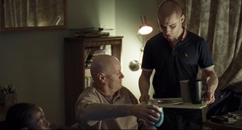 Movie still from “I, Daniel Blake” (2016), directed by Ken Loach – Two men are sitting at a dining room table; Medium shot, Over the shoulder angle