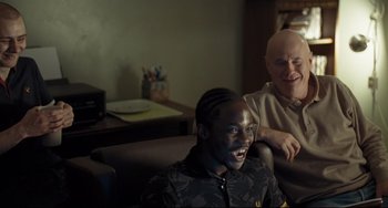 Movie still from “I, Daniel Blake” (2016), directed by Ken Loach – Two men sitting in a living room next to each other; Medium shot, Over the shoulder angle