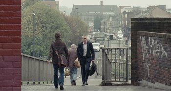 Movie still from “I, Daniel Blake” (2016), directed by Ken Loach – Two men walking down a sidewalk near a street; Wide shot, Low angle