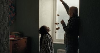 Movie still from “I, Daniel Blake” (2016), directed by Ken Loach – A man and a girl playing with a string of food; Medium shot, Low angle