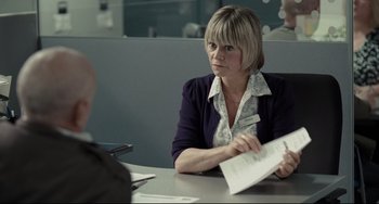 Movie still from “I, Daniel Blake” (2016), directed by Ken Loach – A woman sitting at a table with papers in her hands; Medium shot, Over the shoulder angle
