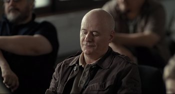 Movie still from “I, Daniel Blake” (2016), directed by Ken Loach – A bald man sitting in front of a group of people; Medium shot, Over the shoulder angle