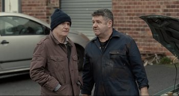 Movie still from “I, Daniel Blake” (2016), directed by Ken Loach – A couple of men standing next to each other; Medium shot, Over the shoulder angle