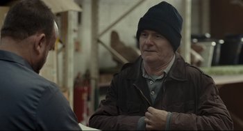 Movie still from “I, Daniel Blake” (2016), directed by Ken Loach – An older man wearing a brown jacket and a black hat; Medium shot, Over the shoulder angle